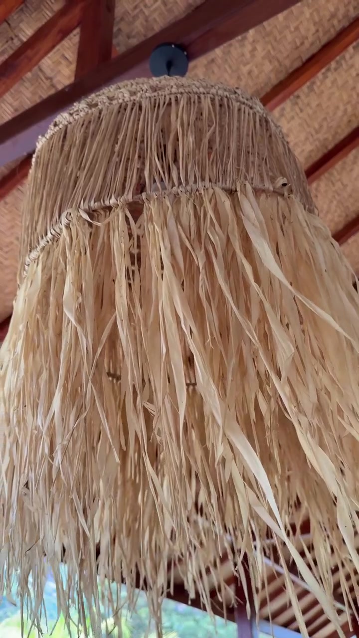 Pantalla de lámpara de paja natural meciéndose suavemente en un entorno tropical