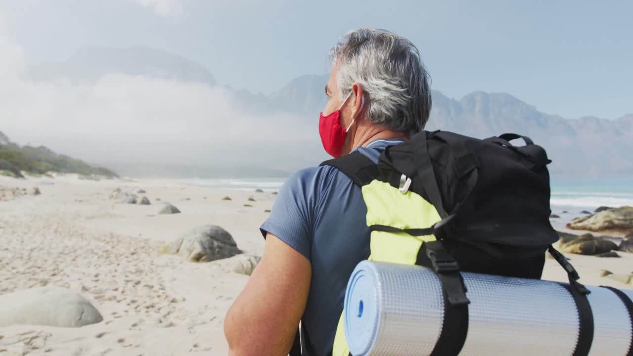 hombre excursionista mayor con máscara facial con mochila caminando mientras caminaba por la playa.