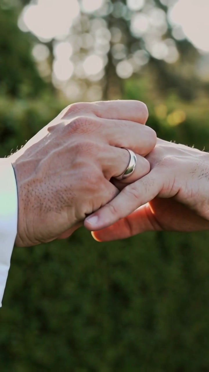 Vertical video: Giver holding partner hand sliding ring in hedge, sealing bond, white cuff visible