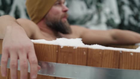 caucasian man sitting in wooden barrel with frozen water.