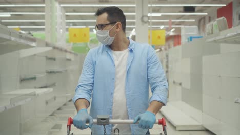 retrato de un hombre descontento con una máscara y guantes contra el fondo de estantes vacíos de la tienda