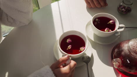 people drink tea with rose buds in cups closeup. couple enjoys romantic breakfast drinking tea with flowers at home in morning. perfect date atmosphere