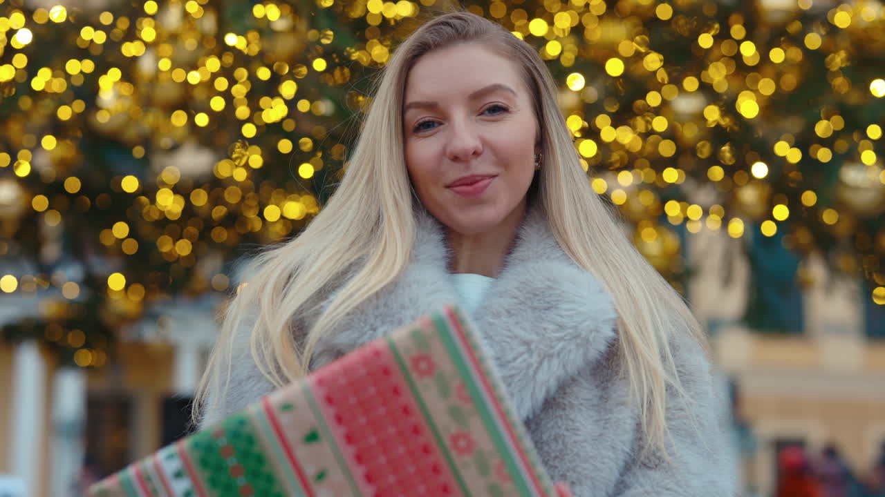Woman Holding a Christmas Gift in Front of a Christmas Tree