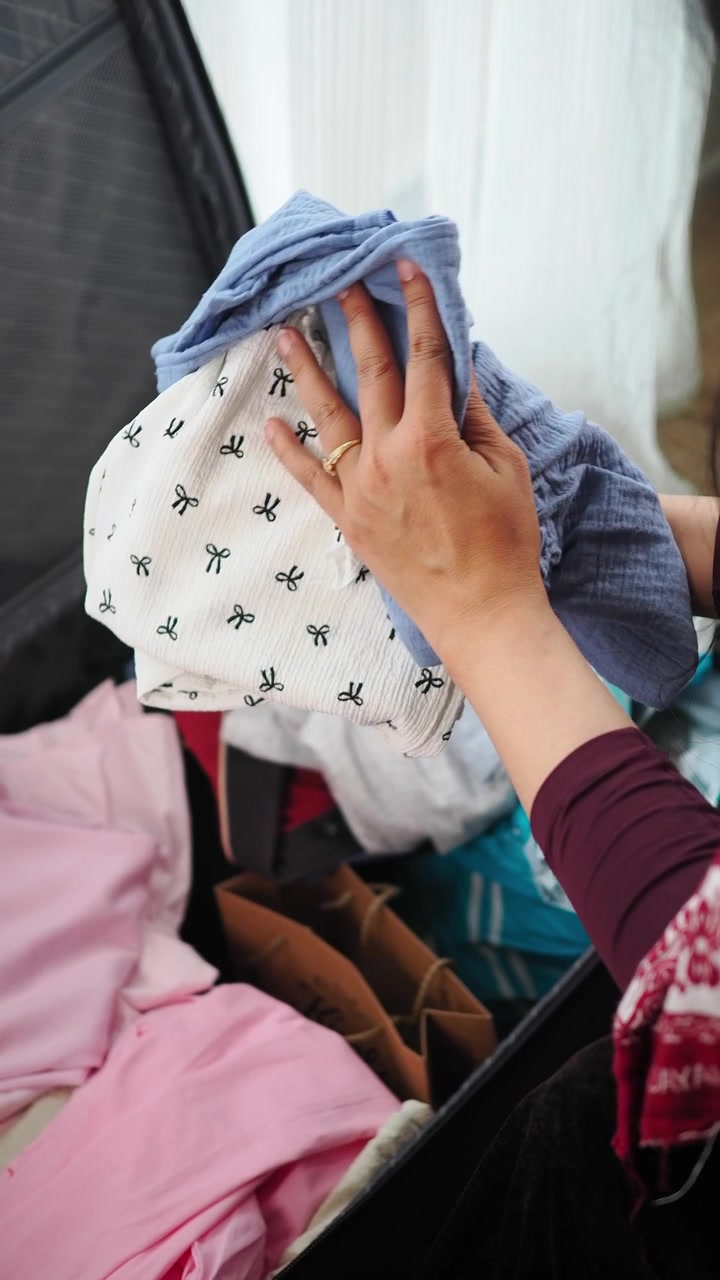 Person Packing Baby Clothes Into A Suitcase