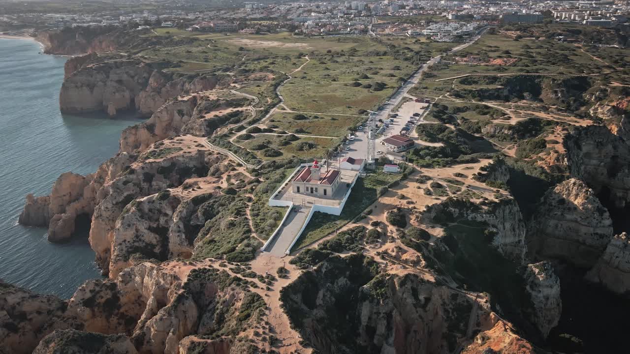 Camera spirals around Ponta da Piedade lighthouse, revealing sculpted cliffs, winding trails, and the sparkling coastline in sweeping sunlit motion