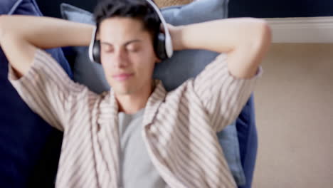 happy biracial man wearing headphones lying on couch relaxing and smiling, slow motion