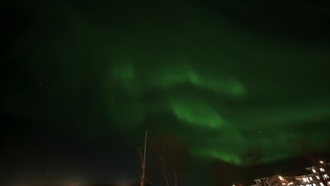 Panning-shot-of-lighting-Selfoss-City-with-buildings-and-northern-lights-at-night-sky-in-Iceland