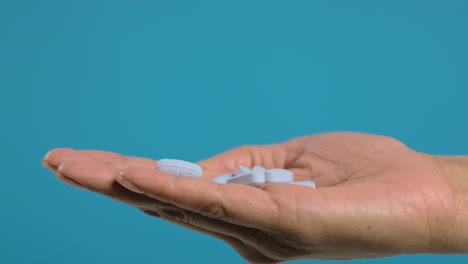 close up de las píldoras que caen en la mano de la mujer contra un fondo azul