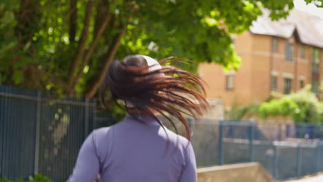 rear view of young woman exercising running along urban street wearing wireless earbuds 1