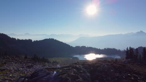 beautiful aerial reveal of mountain peak lake and sun with hazy mountain landscape background on mount brew in canada bc 4k