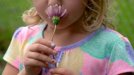 Young-blonde-girl-outside-smells-pink-flower-and-then-gives-charming-happy-smile,-close-up-slow-motion