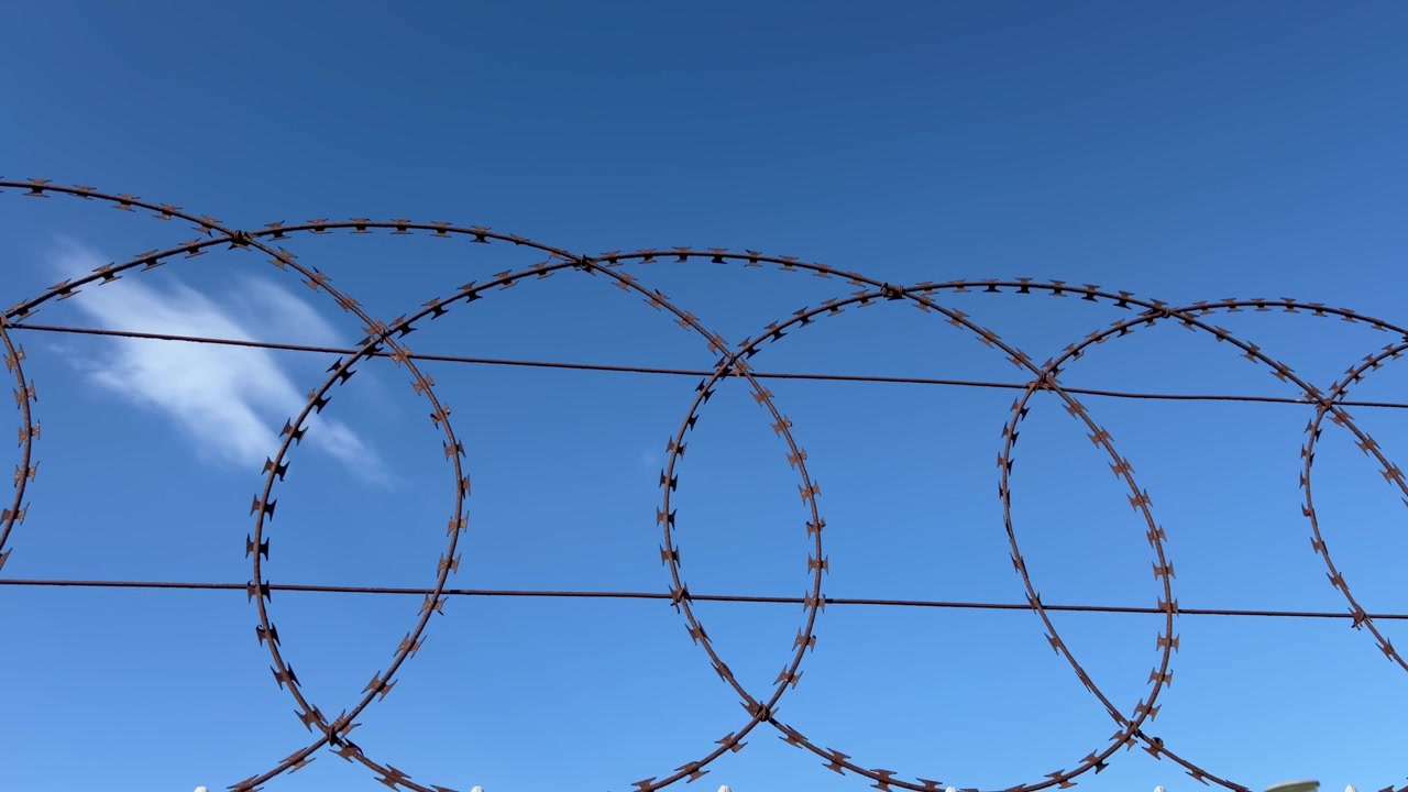 A barbed wire fence against a blue sky.