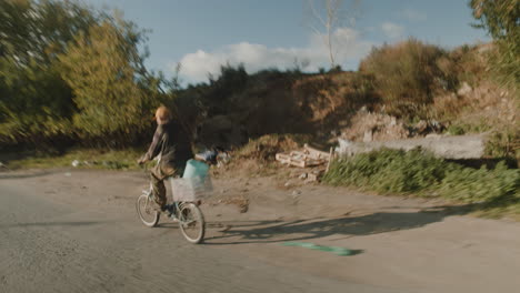 man cycling on a rural road through a trash-filled area