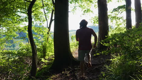 young man with red tshirt is running barefoot in slow motion out of a dark forest towards a bright and sunny meadow