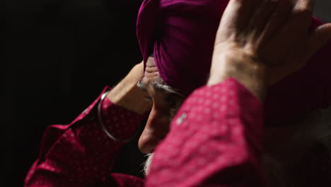 close up low key studio lighting shot of senior sikh man with beard tying fabric for turban against dark background 9