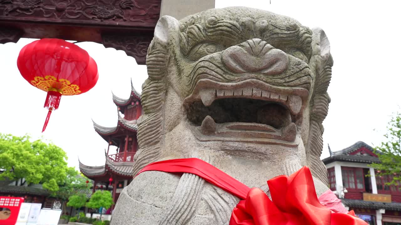 Close up of a stone lion sculpture beside Qibao main gate with a red lantern and pagoda visible in the background. Shanghai, China