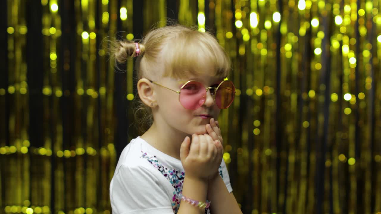 Child smiling, looking at camera, making fly kiss. Girl posing on background with foil curtain