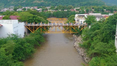 yellow and white bridge connects two sides of city split by tropical river and trees