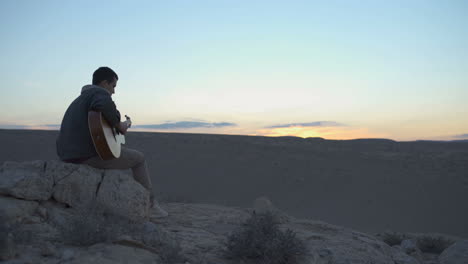 Mann-Spielt-Gitarre-Auf-Einem-Hügel-Während-Des-Sonnenuntergangs-In-Der-Wüste