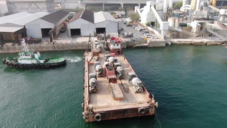 barge loaded with concrete mixer trucks pulled to port by a tugboat in hong kong bay, aerial view