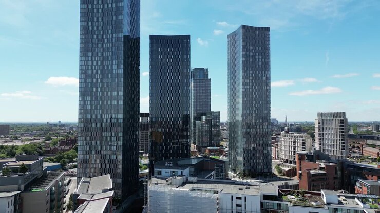 Volo di drone aereo appena sopra i tetti che mostra i grattacieli delle Deansgate South Towers con una vista dello skyline in una giornata di sole luminoso.