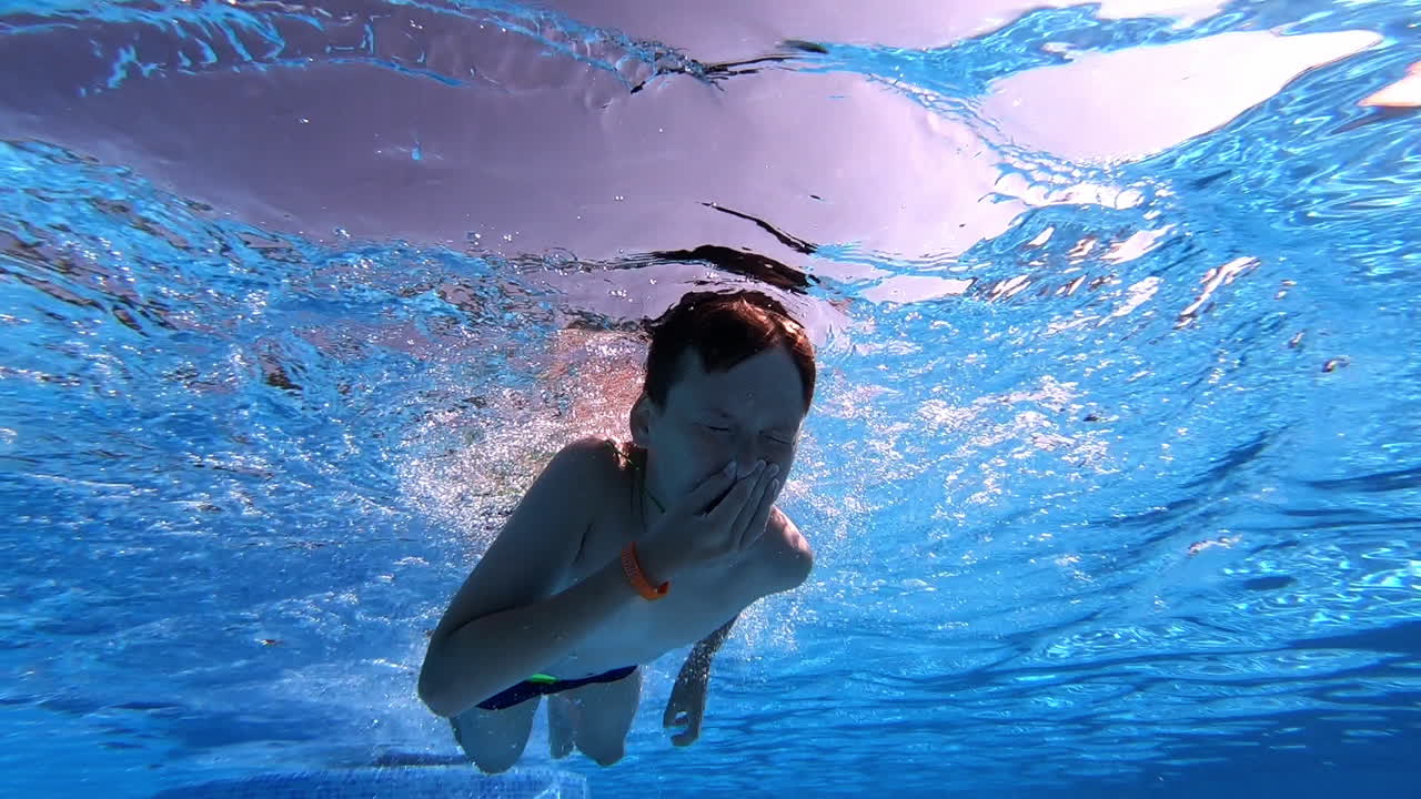 Underwater video of a boy swimming in blue clear water. Little boy dives under the water with closed eyes in the swimming pool.
