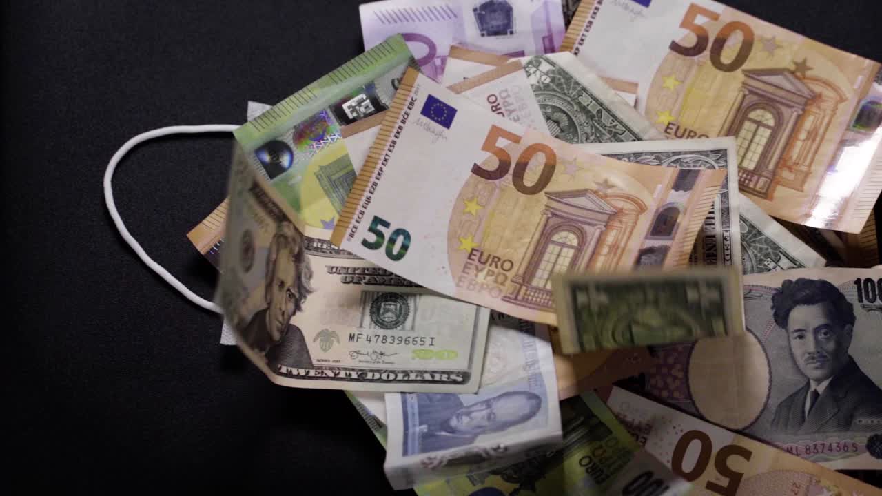 En ansiktsmaske ligger under sedler av dollar, euro, yen og pund. Verdensomspennende krise. Koronakrise. Finanskrise. Kollaps. Arbeidsledighet. Resesjon, børskrakk.
