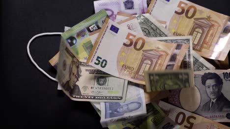 a face mask lies under banknotes of dollar, euro, yen and pound. worldwide crisis. corona crisis. financial crisis. collapse. unemployment. recession, crash stock market