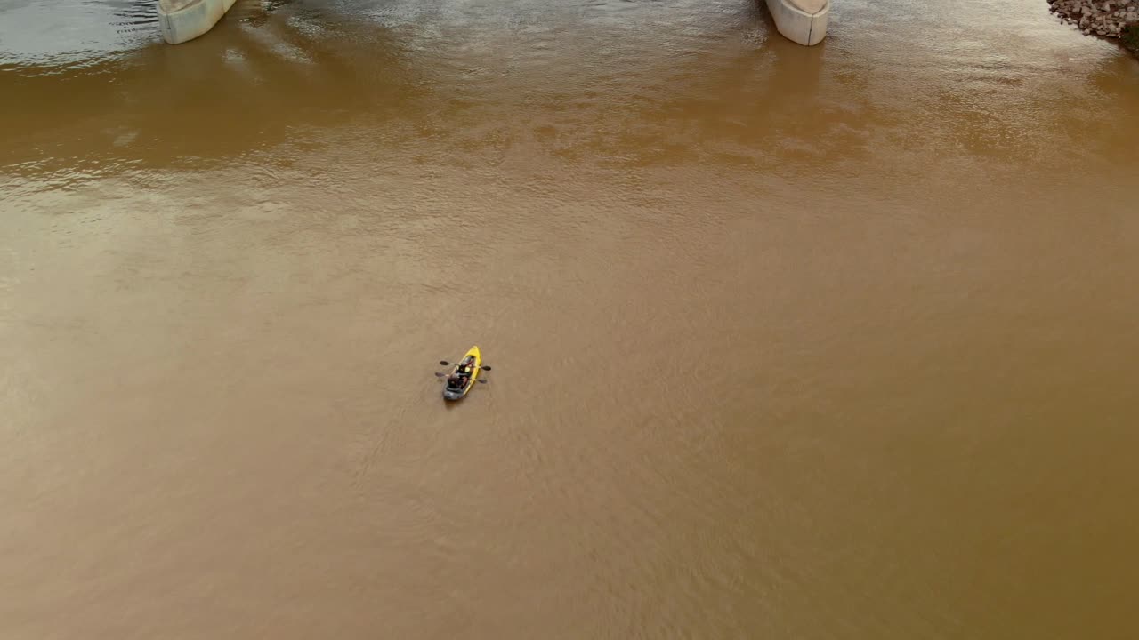 Riprese aeree dall'alto di un kayak biposto che si avvicina pagaiando verso un ponte nelle acque torbide e marroni del fiume Ohio