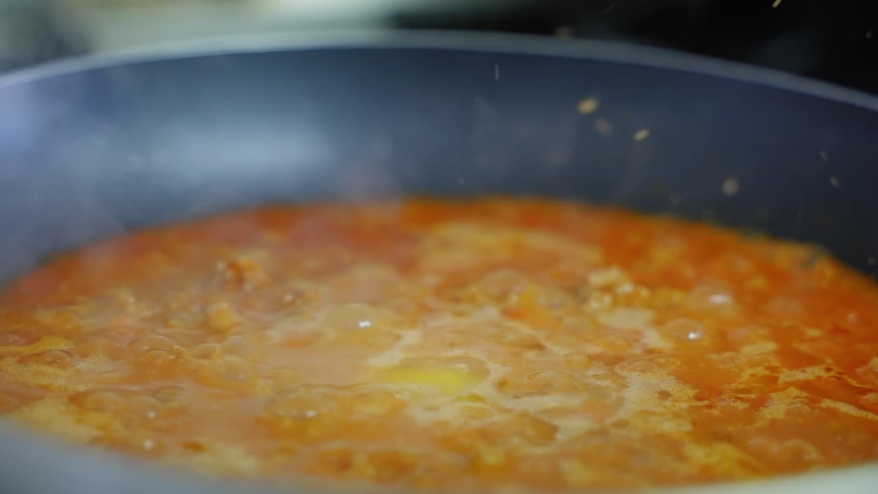 Primo piano di ragù alla bolognese che sobbolle in una padella calda.