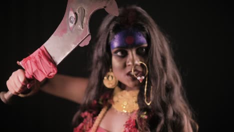 live indian goddess kali looks at camera with sword, indian goddess cosplay with long hair and dark background