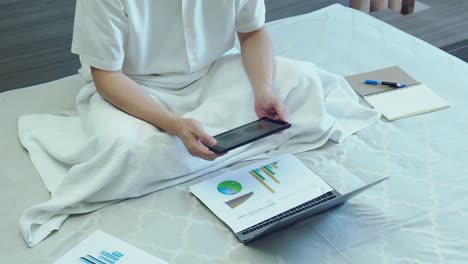 asian business man work with tablet above paper chart or graph on bed