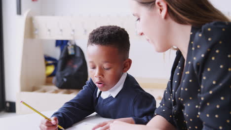 Young-female-primary-school-teacher-working-one-on-one-with-a-schoolboy-in-a-classroom,-close-up