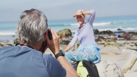 hombre excursionista senior tomando fotos de mujer excursionista senior usando una cámara digital en la playa.