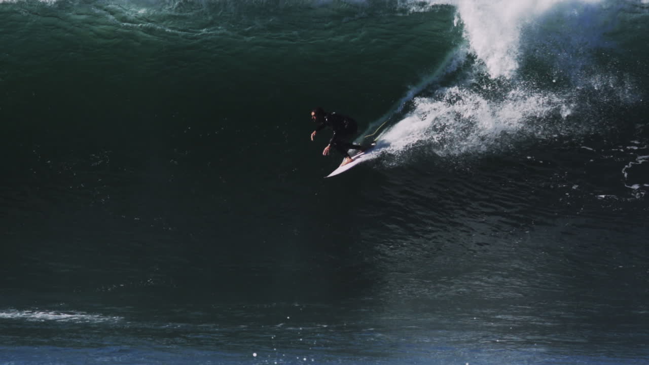 Surfer emerges from barrel under overcast light as wave closes with frothy crash