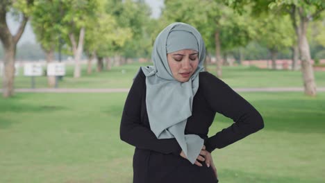 sick muslim woman suffering from back pain in park