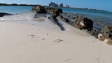 Weißer-Sandstrand-Mit-Ruhigen-Wellen,-Die-Sich-An-Den-Felsen-Waschen