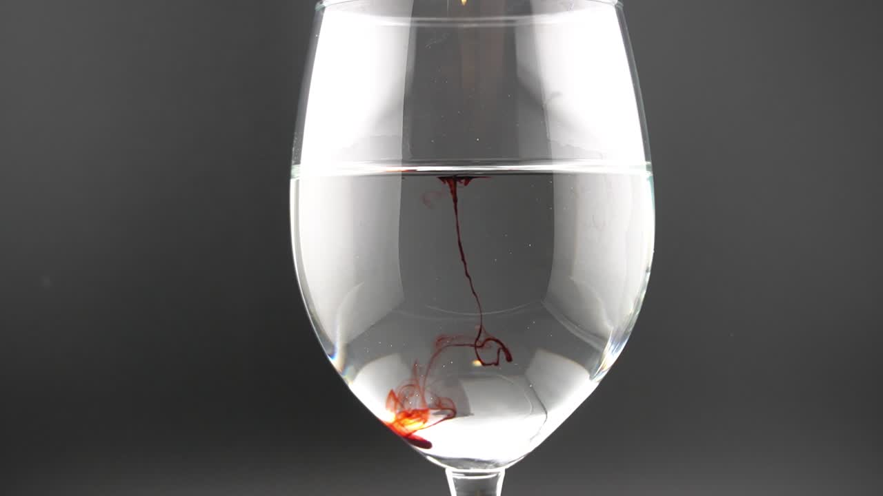 This is a video of a red colored drop, dropping into a wine glass full of water, creating interesting and artistic shapes.
