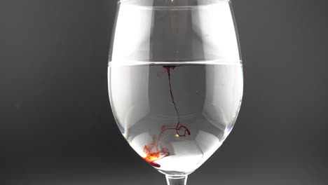 this is a video of a red colored drop, dropping into a wine glass full of water, creating interesting and artistic shapes.