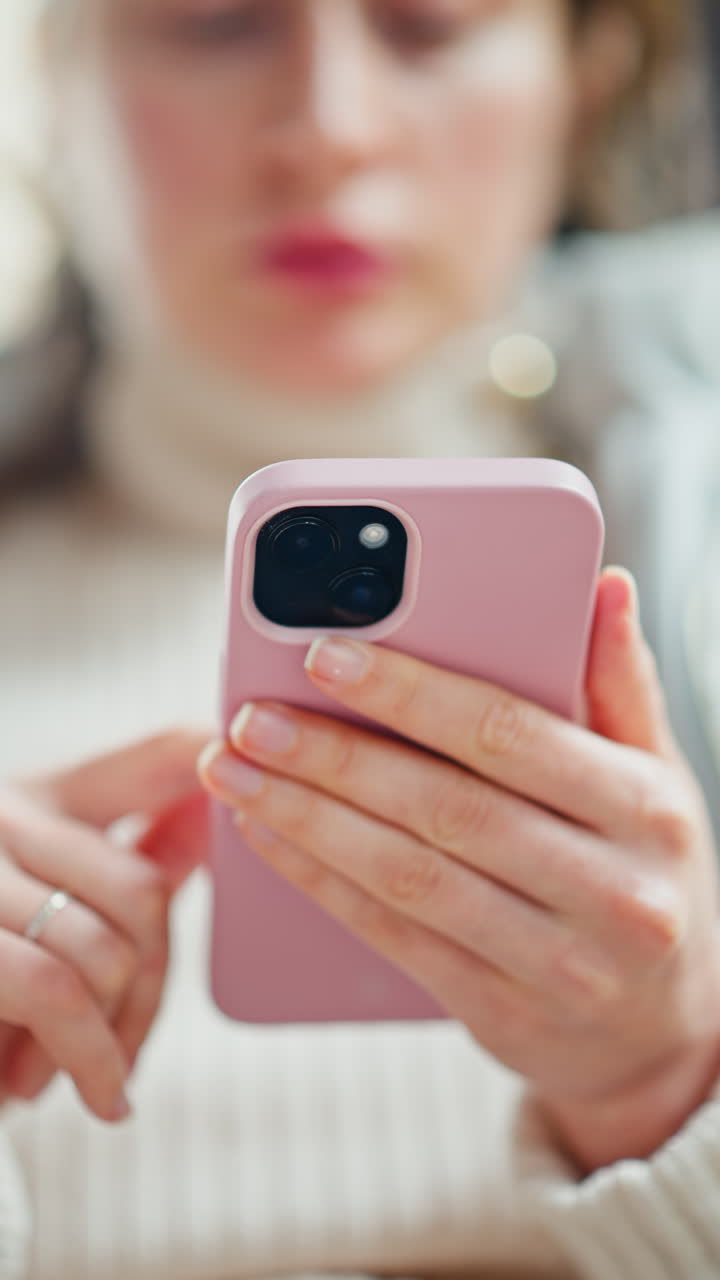 Woman in jacket scrolling through her phone at a cafe. Vertical