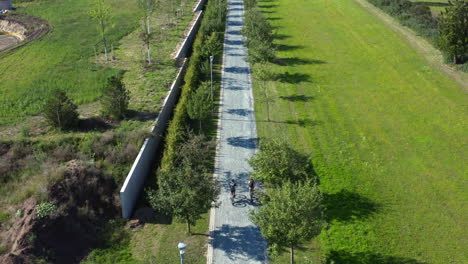 Couple-cycling-side-by-side-on-tree-alley-road-in-countryside,-drone