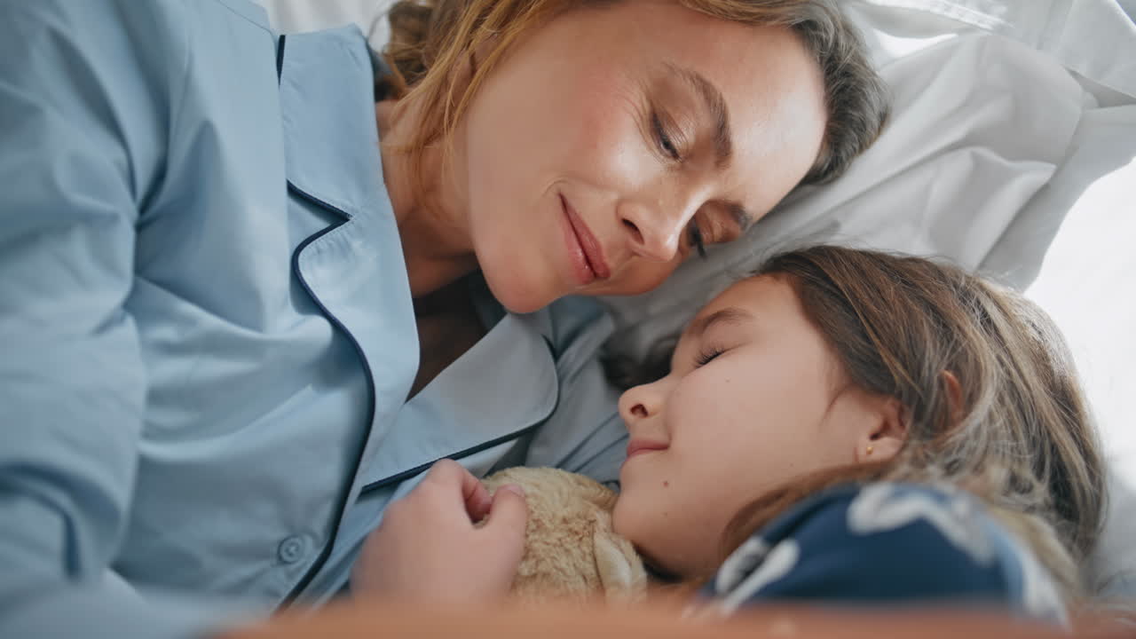 Awake parent toddler bonding cozy bed in pyjamas closeup. Woman stroking girl