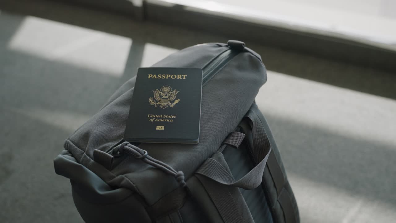 Backpack with passport in airport or train terminal waiting to board sitting in lounge or waiting area during daytime by glass window as sun creates shadows on ground. Traveling to work or vacation
