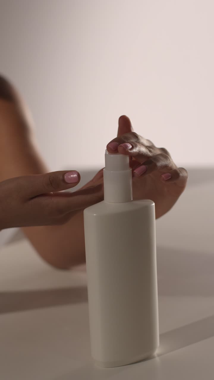 fotografía de belleza de estudio de cuidado de la piel de una mujer dispensando crema hidratante de la botella a la mano