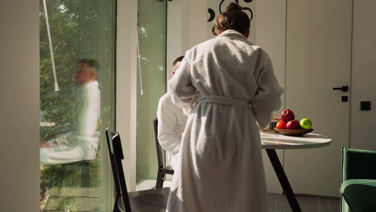 부 테이블에 앉아있는 남자와 함께하는 여자. 테리 욕조를 입은 여자친구가 아침 차를 함께 나누기 위해 테이블에서 앉아 있는 남자친구에게 온다. 아침 일상