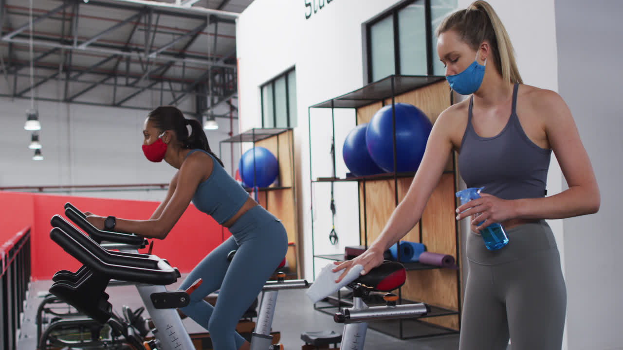 Caucasian woman disinfecting exercise bike saddle at gym