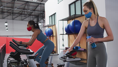 Caucasian-woman-disinfecting-exercise-bike-saddle-at-gym