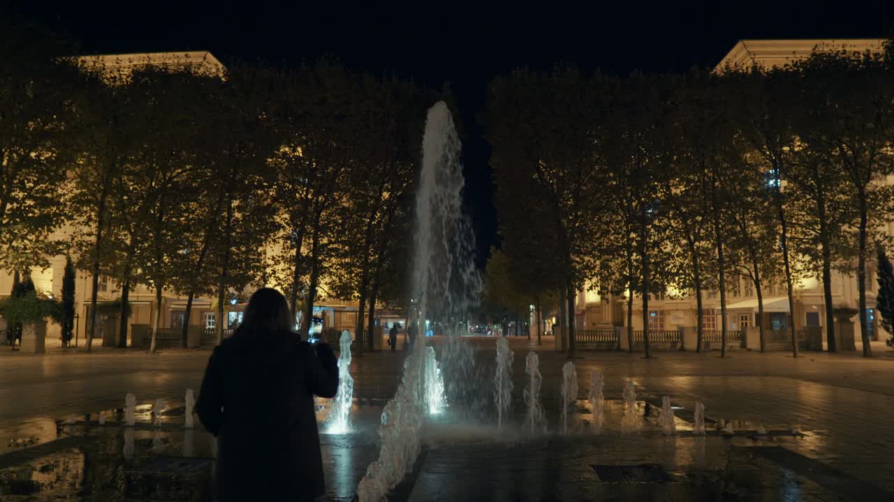 la niña está disparando a la pequeña fuente en el parque por la noche