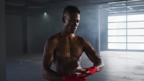 Hombre-Afroamericano-Sin-Camisa-Envolviéndose-Las-Manos-Para-Boxear-En-Un-Edificio-Urbano-Vacío