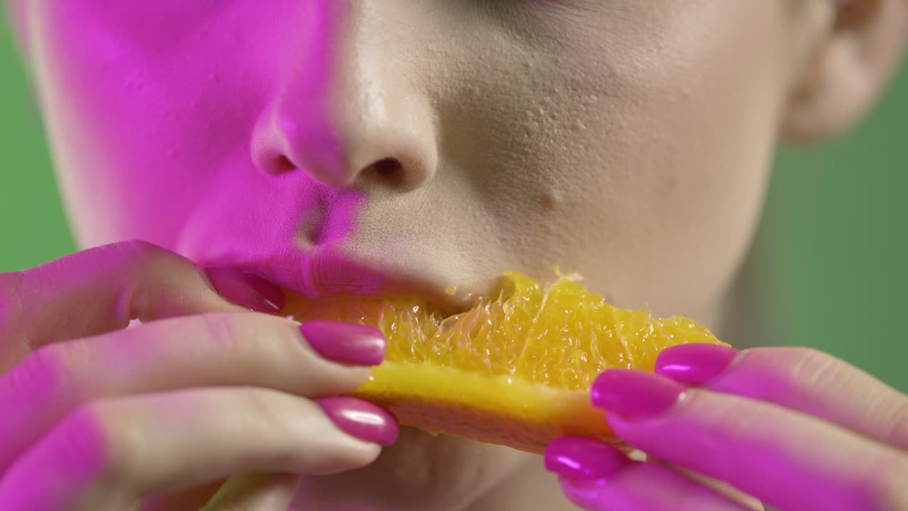 cerca de la cara y la boca de la mujer, tomando un bocado y comiendo una jugosa rebanada de naranja, colorida toma de estudio